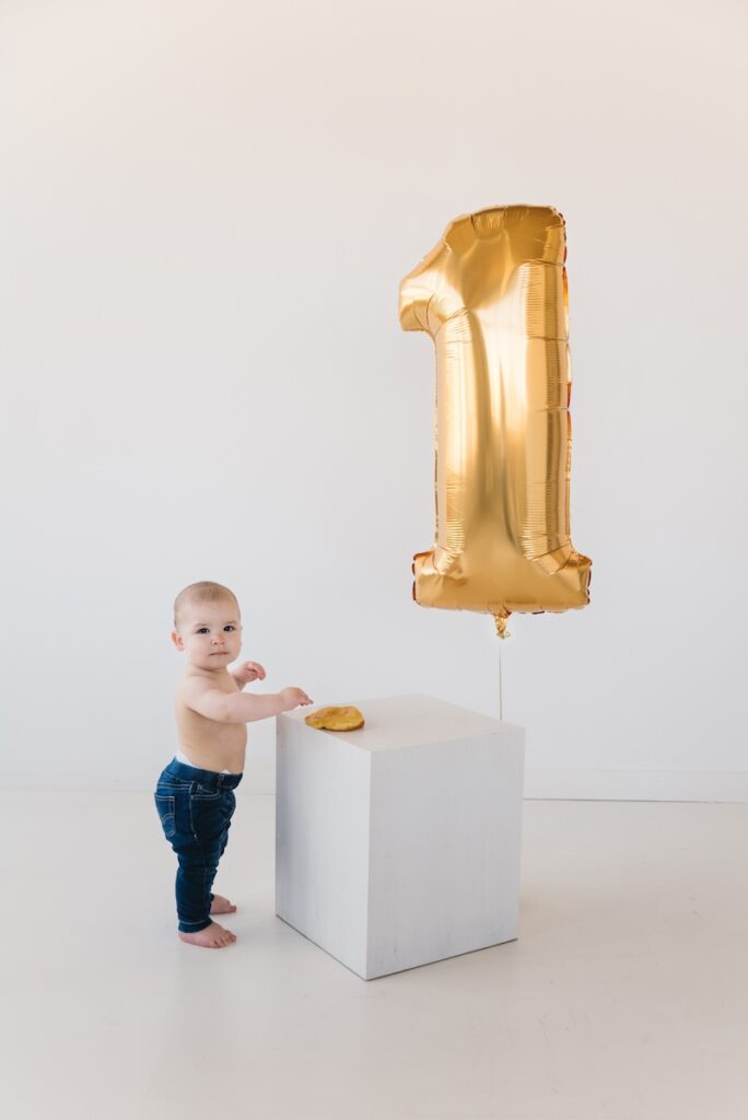baby photograph of 1 year old in blue jeans and gold 1 balloon